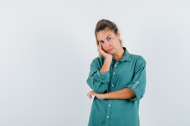 Jonge vrouw leunend wang op palm terwijl denken over iets in groene blouse en peinzend kijken