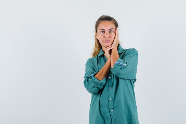 Jonge vrouw leunende palm op wang in groene blouse en op zoek ernstig