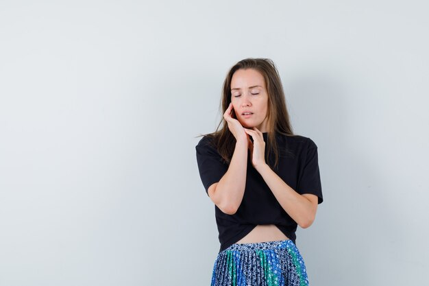 Jonge vrouw leunende wang op palm in zwart t-shirt en blauwe rok en ziet er aantrekkelijk uit