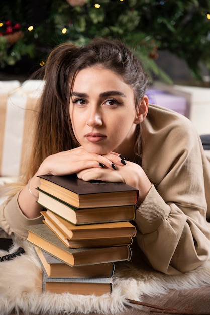 Gratis foto jonge vrouw liggend op pluizig tapijt met boeken.