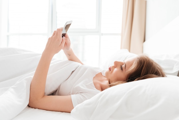 jonge vrouw ligt in bed op zoek opzij chatten