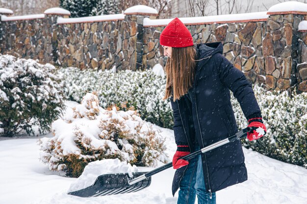Jonge vrouw maakt sneeuw in de tuin schoon bij sneeuwweer