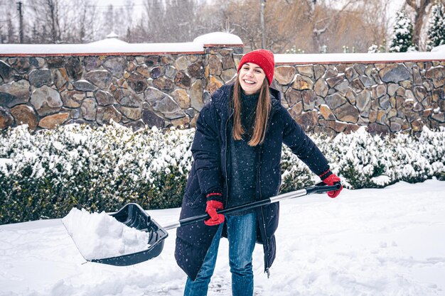 Jonge vrouw maakt sneeuw in de tuin schoon bij sneeuwweer
