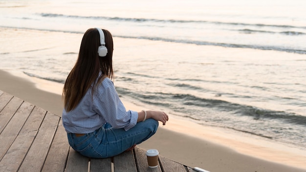 Jonge vrouw mediteren naast zee terwijl ze een koptelefoon draagt
