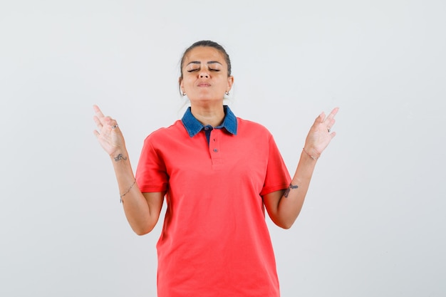 Jonge vrouw mediteren terwijl ze ogen in een rood shirt sluit en er ontspannen uitziet. vooraanzicht.