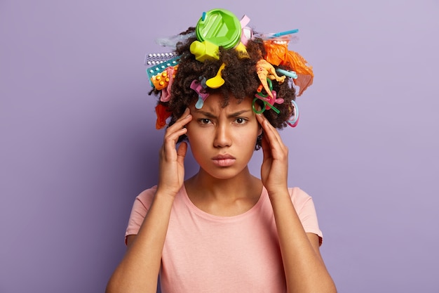 Jonge vrouw met afro-kapsel en plastic afval in haar haar