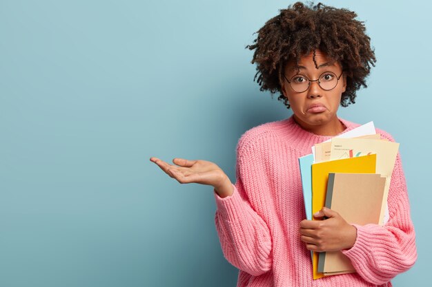 Jonge vrouw met Afro-kapsel roze trui dragen en leerboeken te houden