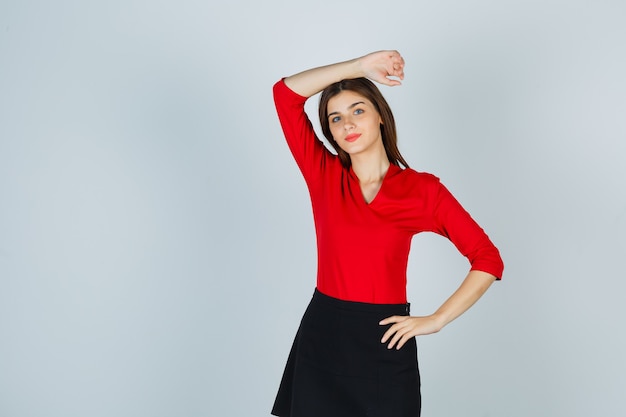 Jonge vrouw met arm boven het hoofd, hand zetten heup in rode blouse