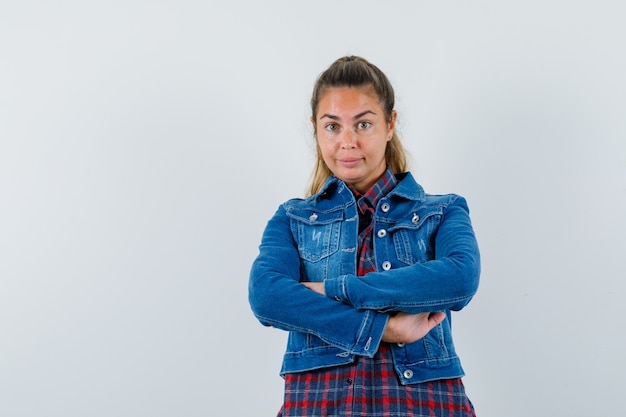 Jonge vrouw met armen gevouwen in shirt, jasje en op zoek zelfverzekerd, vooraanzicht.