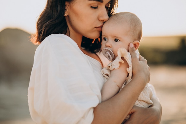 Jonge vrouw met babydochter in drager op de zonsondergang