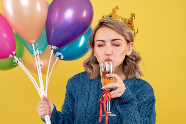 jonge vrouw met ballonnen en glas champagne op geel