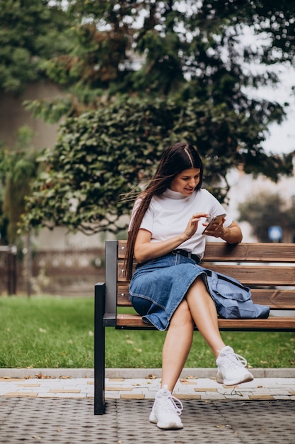 Jonge vrouw met behulp van telefoon en zittend op een bankje in het park