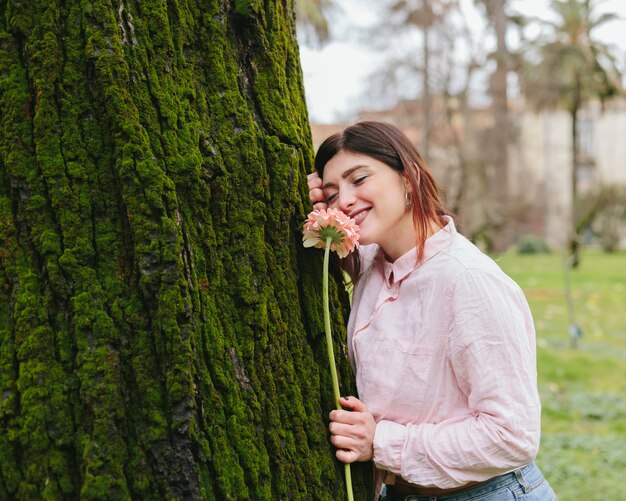 Jonge vrouw met bloem die op boom leunt
