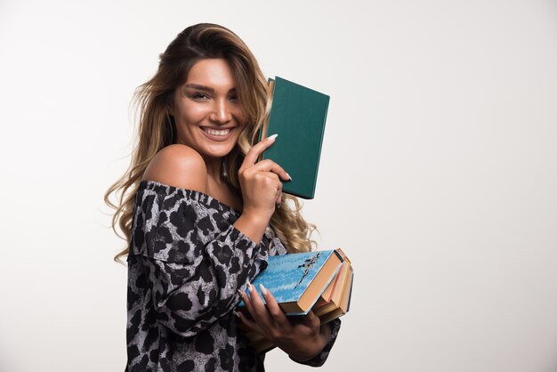 Jonge vrouw met boeken terwijl lachen op witte muur.