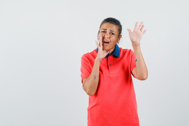 Jonge vrouw met de hand in de buurt van de mond als iemand belt en stopbord in rood t-shirt toont en er mooi uitziet, vooraanzicht.