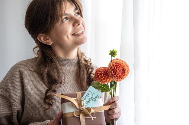 Jonge vrouw met een cadeau voor moederdag en een boeket bloemen in haar handen