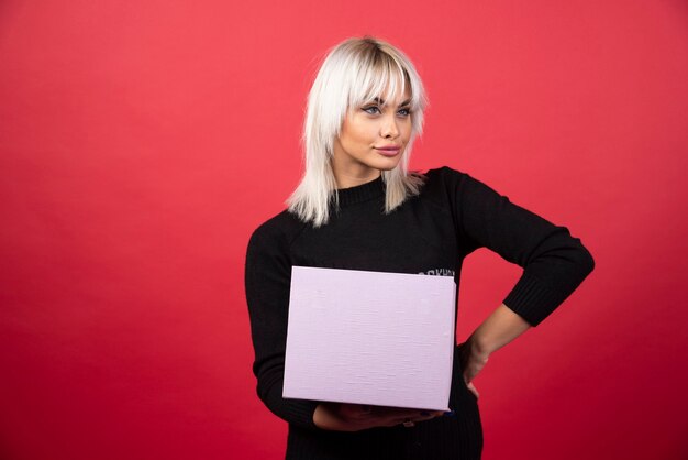 Jonge vrouw met een cadeautje op een rode muur.