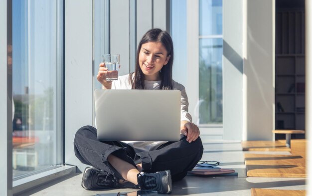 Gratis foto jonge vrouw met een glas water voor een laptop in de ochtend