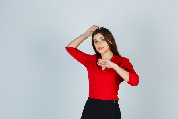 Jonge vrouw met een hand boven het hoofd terwijl poseren in rode blouse