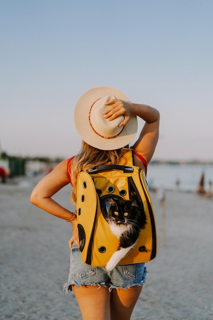jonge vrouw met een kat in een rugzak aan de kust. Reisconcept met een huisdier. Kat in de rugzak met patrijspoort.