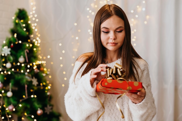 Gratis foto jonge vrouw met een kerstboom binnenshuis