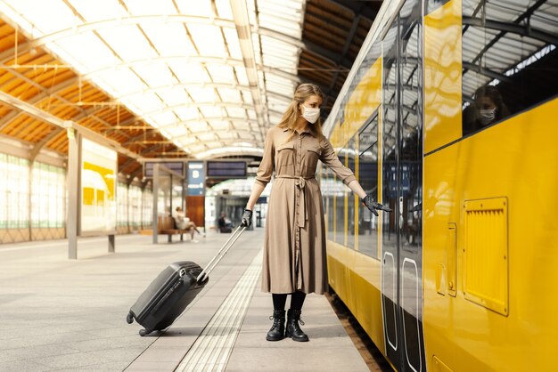 Jonge vrouw met een koffer die een gezichtsmasker en handschoenen draagt en op een trein stapt