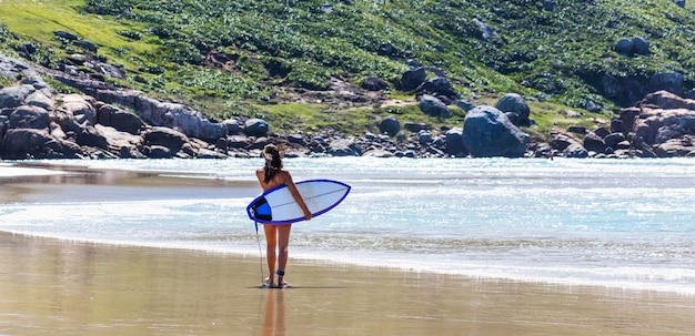 Jonge vrouw met een surfplank aan de zandige kust van de zee Gratis Foto
