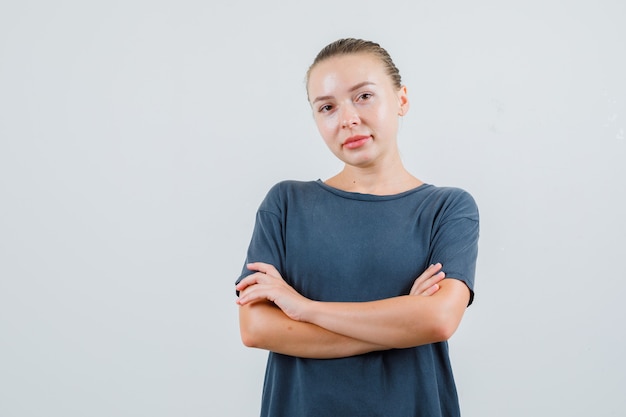 Jonge vrouw met gekruiste armen in grijs t-shirt en op zoek zelfverzekerd