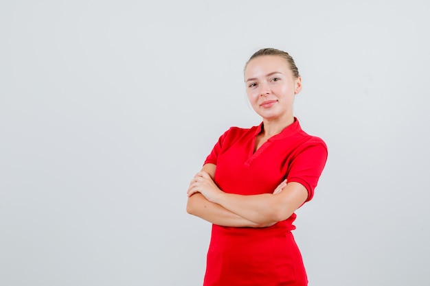 Jonge vrouw met gekruiste armen in rood t-shirt en op zoek vrolijk