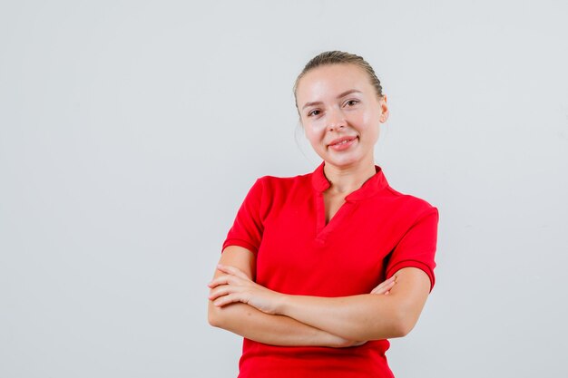 Jonge vrouw met gekruiste armen in rood t-shirt en op zoek vrolijk