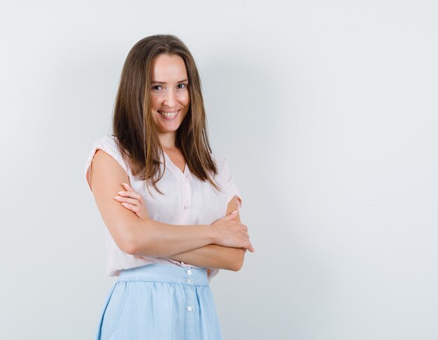 Jonge vrouw met gekruiste armen in t-shirt, rok en op zoek vrolijk. vooraanzicht.