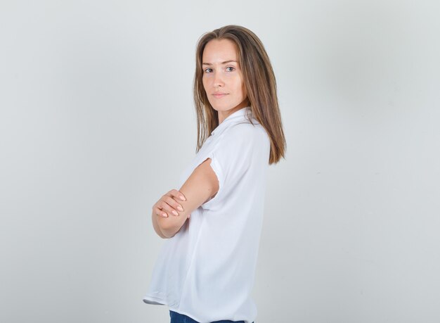 Jonge vrouw met gekruiste armen in wit t-shirt en op zoek zelfverzekerd