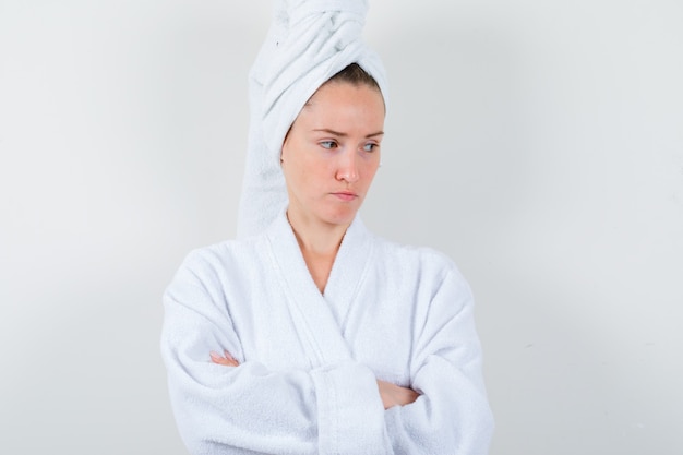 Jonge vrouw met gekruiste armen in witte badjas, handdoek en op zoek boos, vooraanzicht.