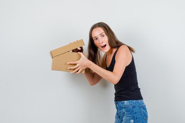 Jonge vrouw met geopende kartonnen doos in hemd, korte broek en op zoek opgewonden.