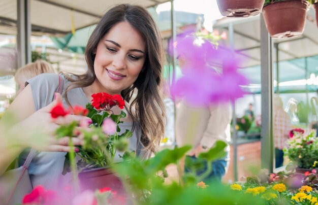 Jonge vrouw met geranium in kleipot bij tuincentrum. Jonge vrouw winkelen bloemen op markt tuin centrum