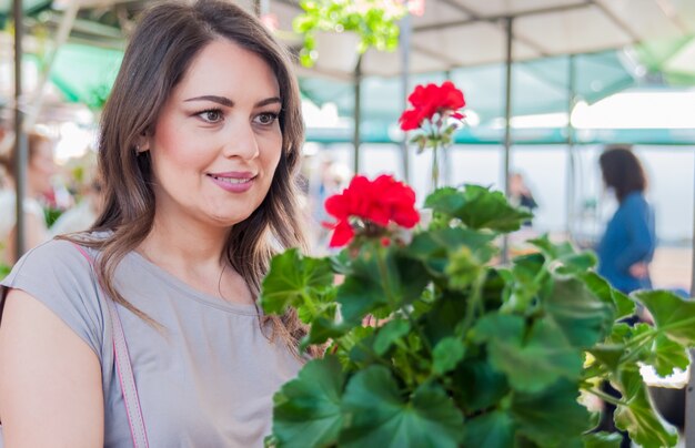Jonge vrouw met geranium in kleipot bij tuincentrum. Tuinieren, planten - vrouw met geranium bloemen
