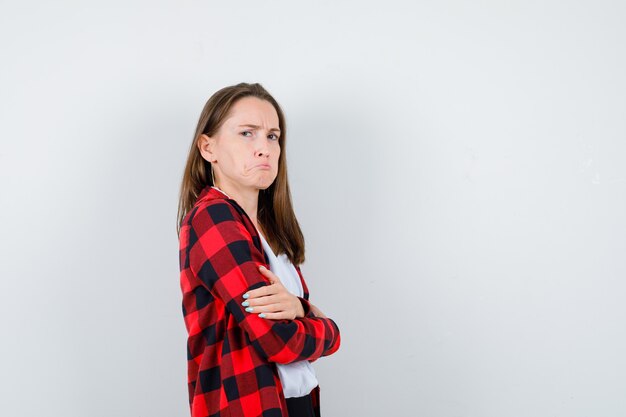 Jonge vrouw met gevouwen armen, gebogen onderlip in vrijetijdskleding en sulky kijkend.