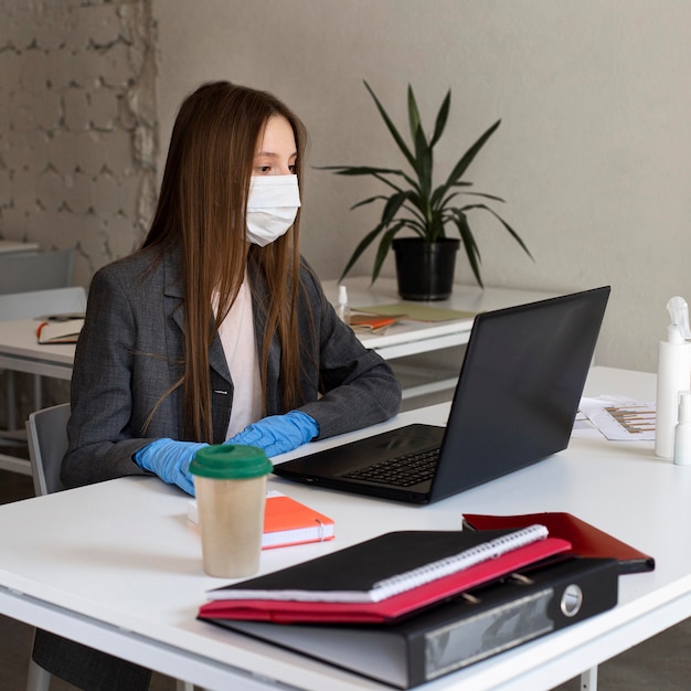 Jonge vrouw met gezichtsmasker op kantoor werken