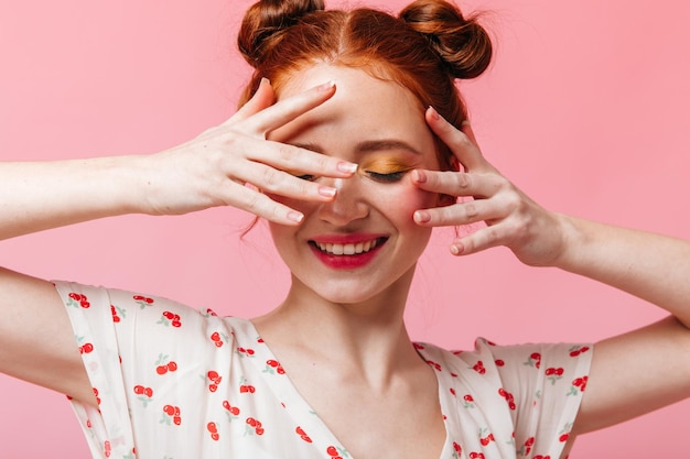 Jonge vrouw met groene ogen glimlacht en bedekt haar gezicht met haar handen poseren op roze achtergrond