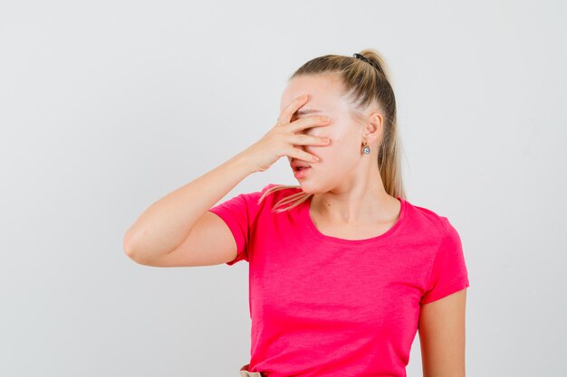 Jonge vrouw met hand op gezicht in t-shirt en op zoek bedroefd