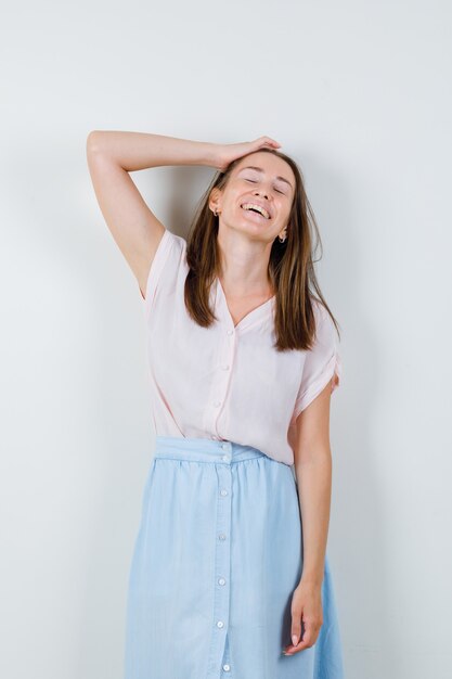 Jonge vrouw met hand op hoofd in t-shirt, rok en schattig kijken. vooraanzicht.