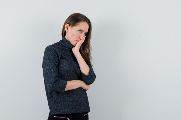 Jonge vrouw met hand op mond in shirt en aarzelend op zoek. vooraanzicht.