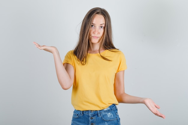 Jonge vrouw met handpalmen gebaren, opties in t-shirt, korte broek proberen te kiezen en op zoek verward