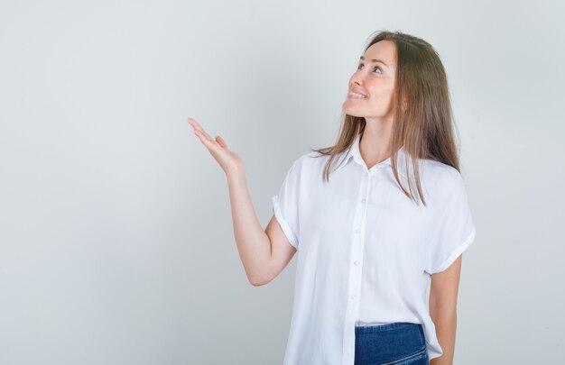 Jonge vrouw met handteken opzoeken in wit t-shirt, spijkerbroek en op zoek vrolijk