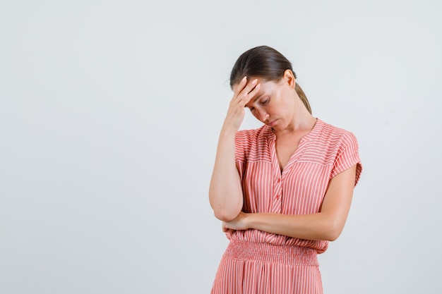 Jonge vrouw met hoofdpijn in gestreepte jurk en op zoek moe. vooraanzicht.