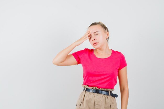 Jonge vrouw met hoofdpijn in t-shirt en broek en op zoek moe