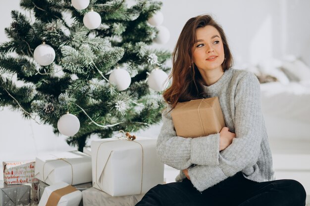 Jonge vrouw met kerstcadeautjes bij de kerstboom