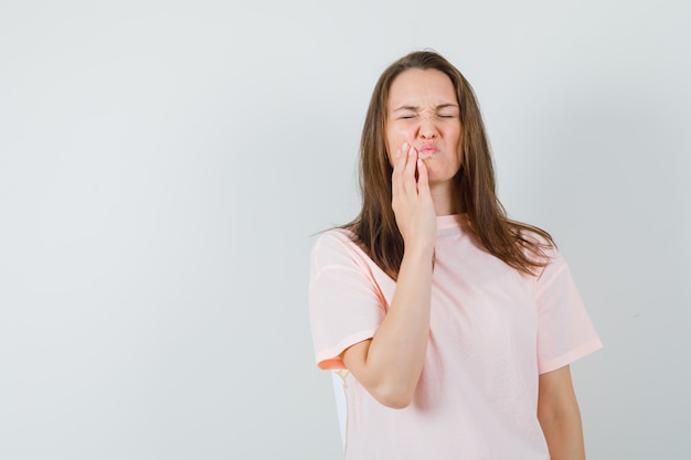 Jonge vrouw met kiespijn in roze t-shirt en ongemakkelijk op zoek.