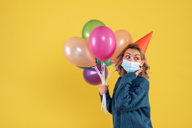 jonge vrouw met kleurrijke ballonnen in masker op geel