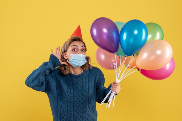 jonge vrouw met kleurrijke ballonnen in masker op geel